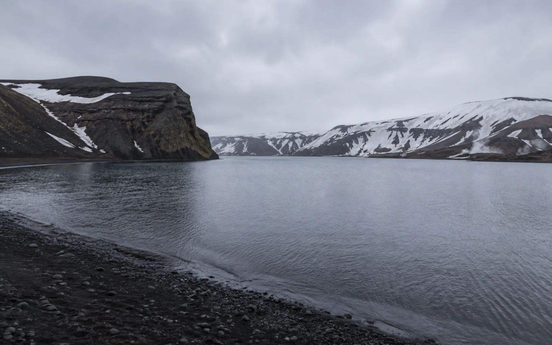 Black volcanic shoreline, snow and geothermal steam inside Deception Island